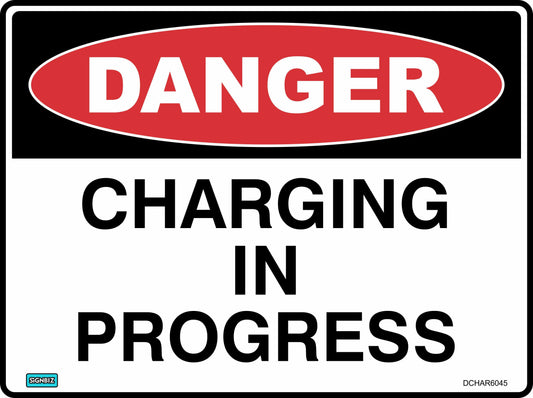 The Danger Charging In Progress sign, compliant with AS NZ 1319-1994, has a red "DANGER" oval at the top and bold black text stating "CHARGING IN PROGRESS," warning that charging is currently underway.