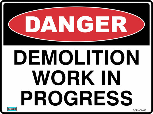 The "Danger Demolition In Progress" sign features a red oval labeled "DANGER" at the top with bold black text on a white background, commonly used as a safety sign at construction sites.