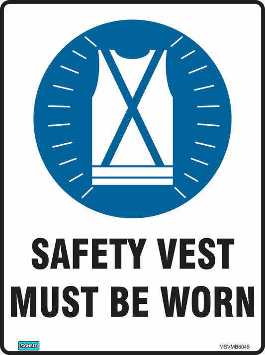 A blue and white "Mand Safety Vest Must Be Worn" sign features a safety vest image and bold black text below, clearly promoting mandatory workplace safety procedures.