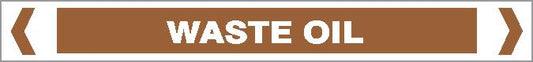 A rectangular brown pipe marker with bold white capitals reading "OILS - WASTE OIL" in the center, bordered by white and brown lines and angle brackets on each side.