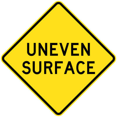 A W5-43 - Uneven Surface sign is a yellow, diamond-shaped road sign featuring the words "UNEVEN SURFACE" in bold black letters.