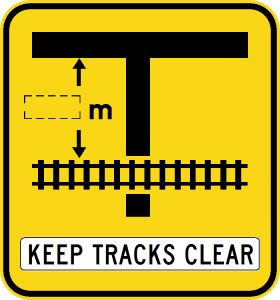 W7-12-3n warning sign: black T-junction meets railroad tracks, top arrow labeled "m," text below says "KEEP TRACKS CLEAR.