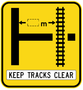 The W7-12-3n(R) sign is a yellow road sign showing a rail crossing at a right 'T' junction, indicating distance with arrows and "m." A white rectangle below says "KEEP TRACKS CLEAR" in black letters.