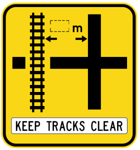 The W7-13-2n(L) sign warns of a rail crossing on a left side road, with arrows showing distance in meters and "KEEP TRACKS CLEAR" text at the bottom.