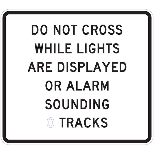 A rectangular W7-14-6 sign reads "DO NOT CROSS WHILE LIGHTS ARE DISPLAYED OR ALARM SOUNDING (2 TRACKS)" in bold, black uppercase letters on a white background with a black border.